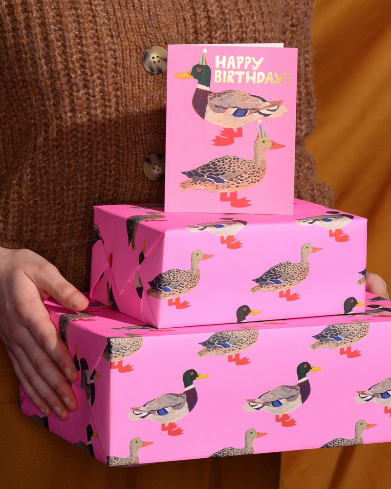 Stack of pink gift boxes with duck pattern, one showing 'Happy Birthday' card.