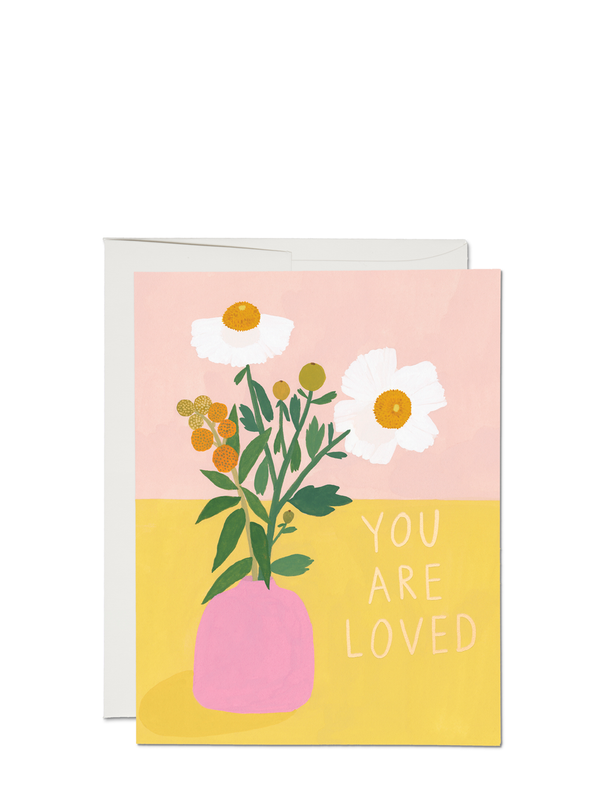 A greeting card with an illustration of white poppies in a pink vase on a yellow background, with the text 'YOU ARE LOVED' displayed.