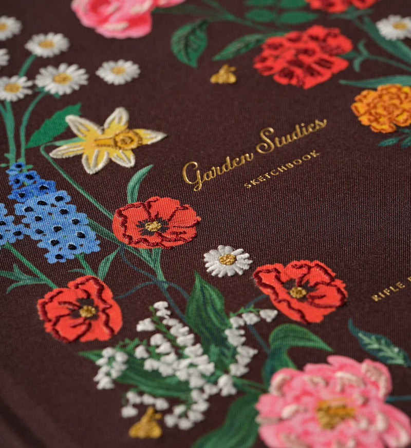 Floral embroidery on a dark fabric background with 'Garden Studios' branding.