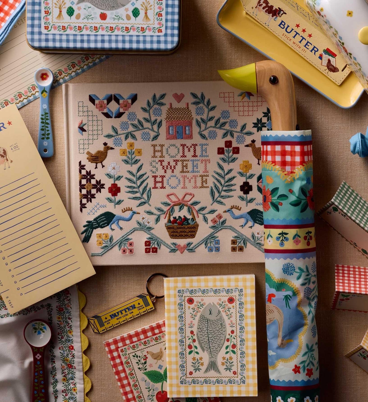 Collection of decorative items including a cross-stitched 'Home Sweet Home' guestbook, a patterned towel, and various small kitchen accessories on a wooden surface.