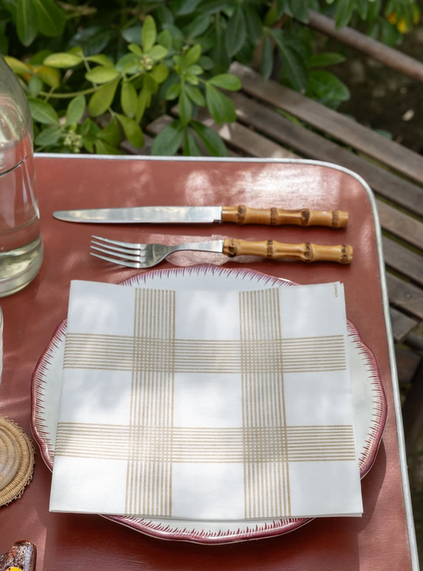 Dinner setting with a checkered napkin on a plate, knife, and fork on a table outdoors.