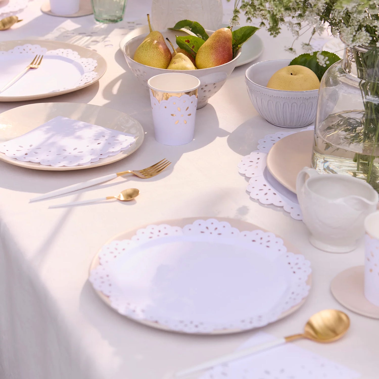 Elegant table setting with white plates, gold cutlery, and pears on a light surface.