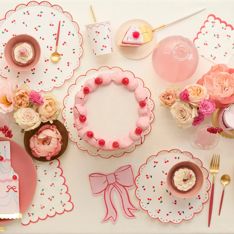 Table setting with pink cake, cupcakes, and floral arrangements on a white tablecloth.