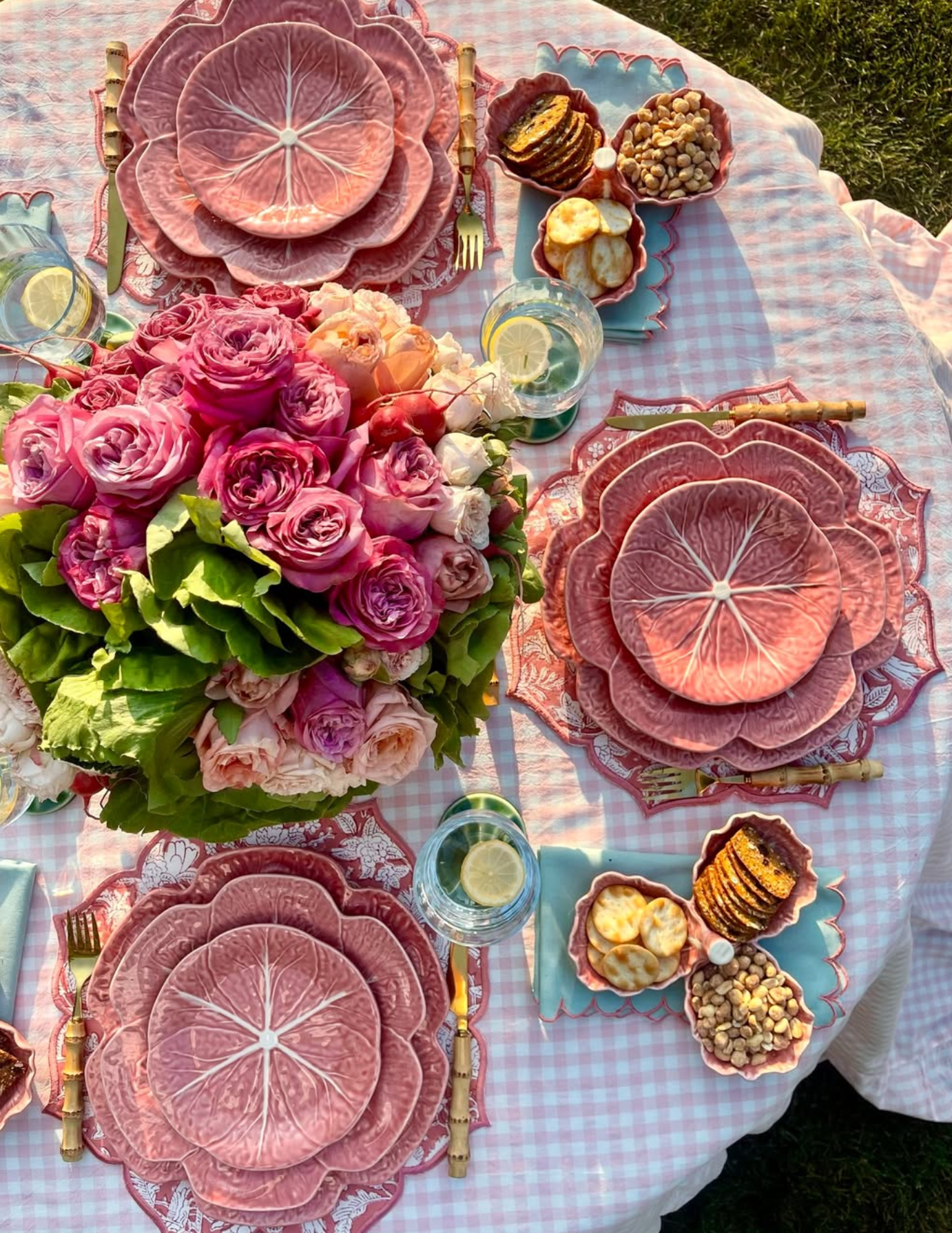 Decorative table setting with pink floral centerpieces and patterned plates on a checkered tablecloth.
