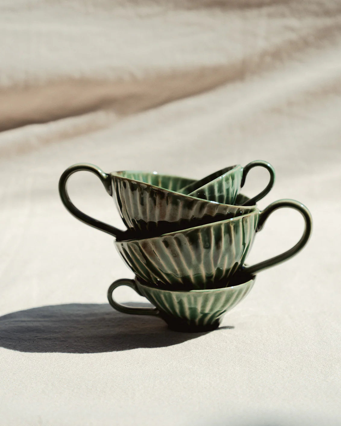 Stack of green ceramic cups on a textured surface