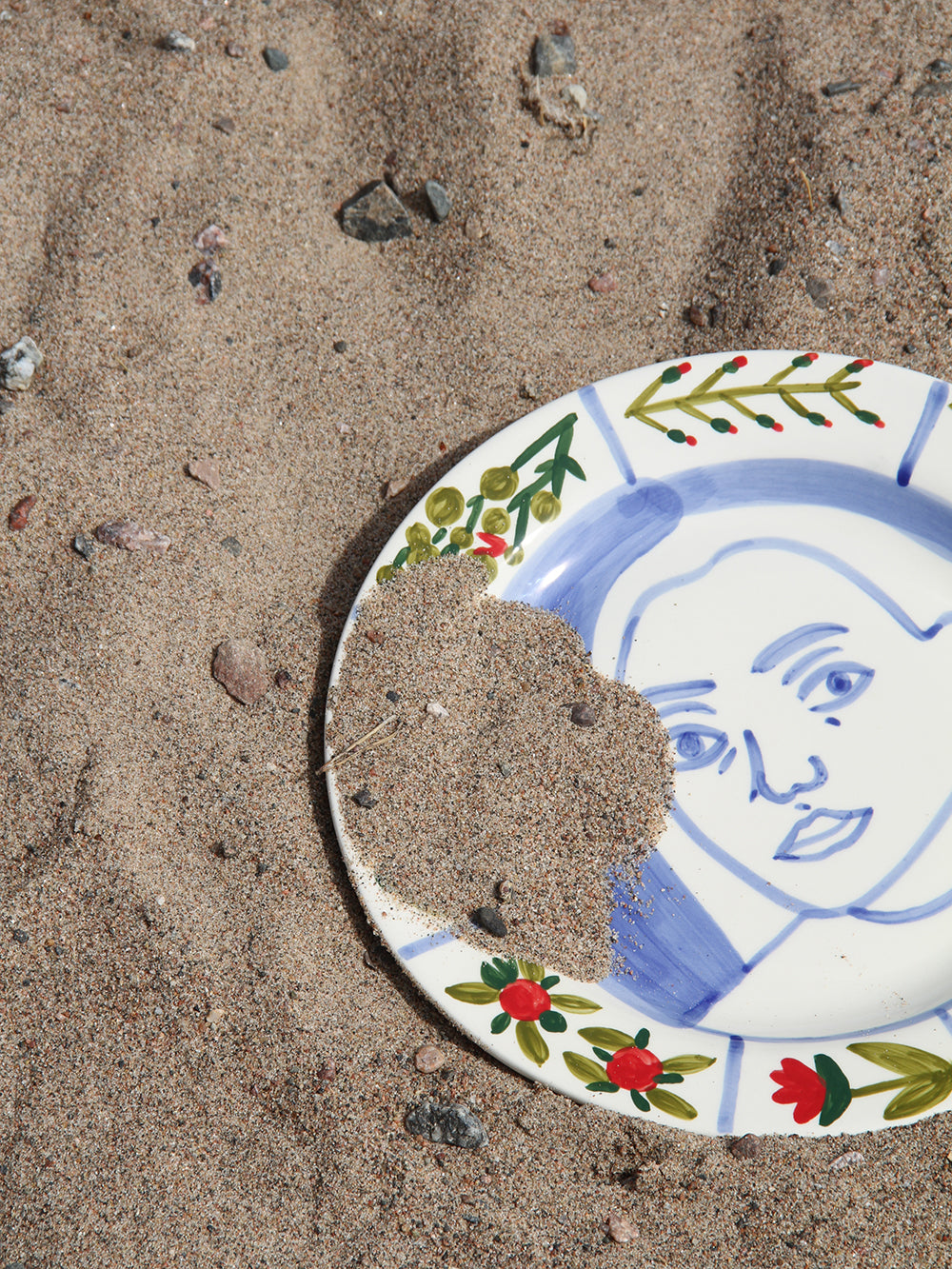 Broken ceramic plate with a face design on a sandy surface