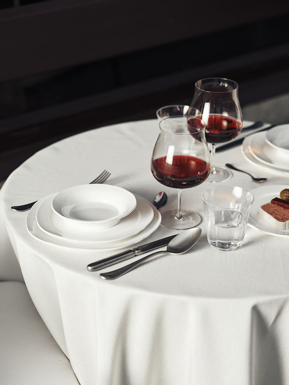 Elegant table setting with white plates, glasses, and cutlery on a white tablecloth.