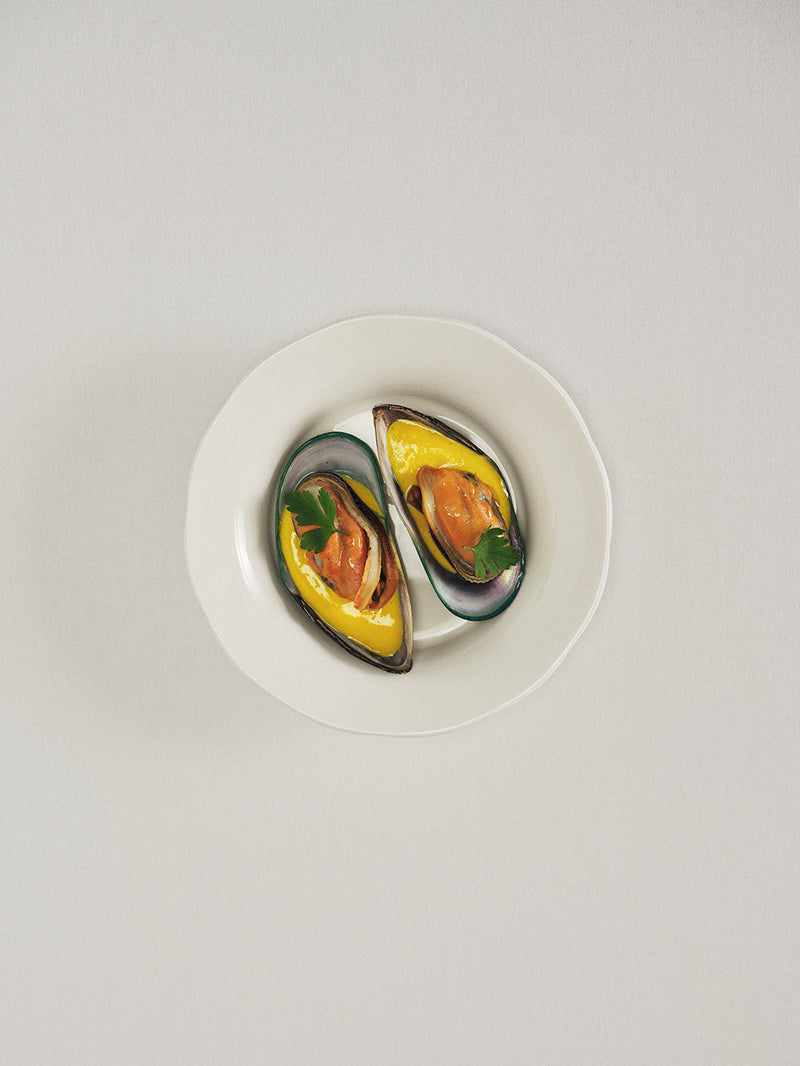 Two mussels in a white dish on a light gray background