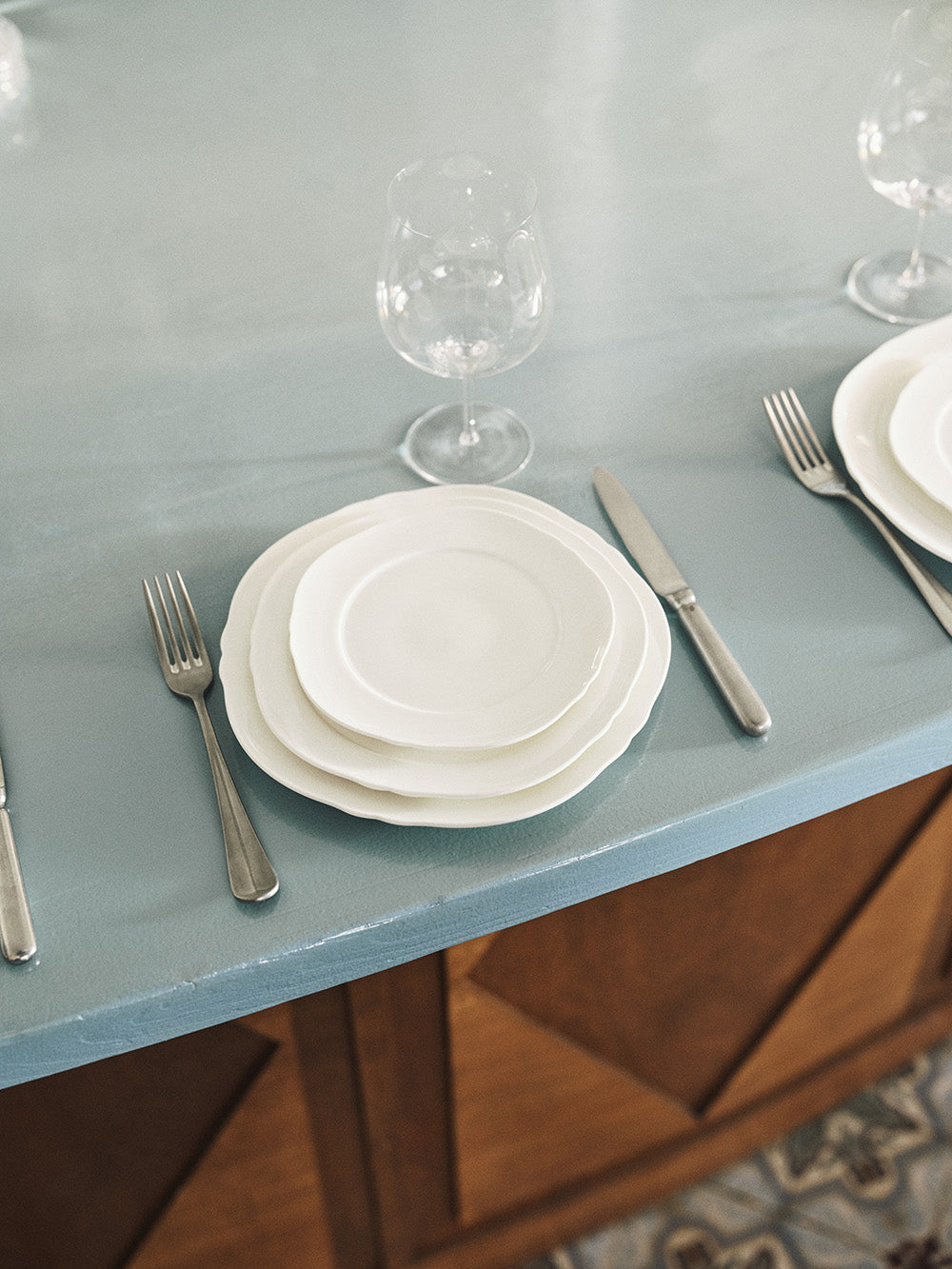 Set of white plates, silverware, and glasses on a light blue tablecloth.