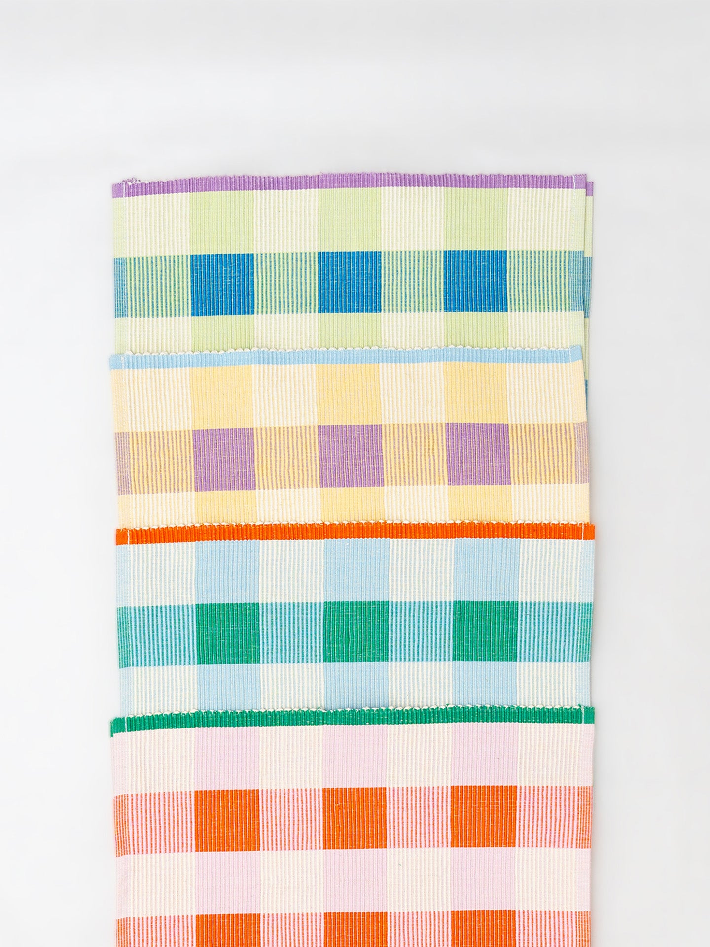 A set of woven placemats  featuring a multicolor plaid and checkered pattern with stripes of purple, blue, yellow, green, orange, and pink on a white base, shown against a plain white background.
