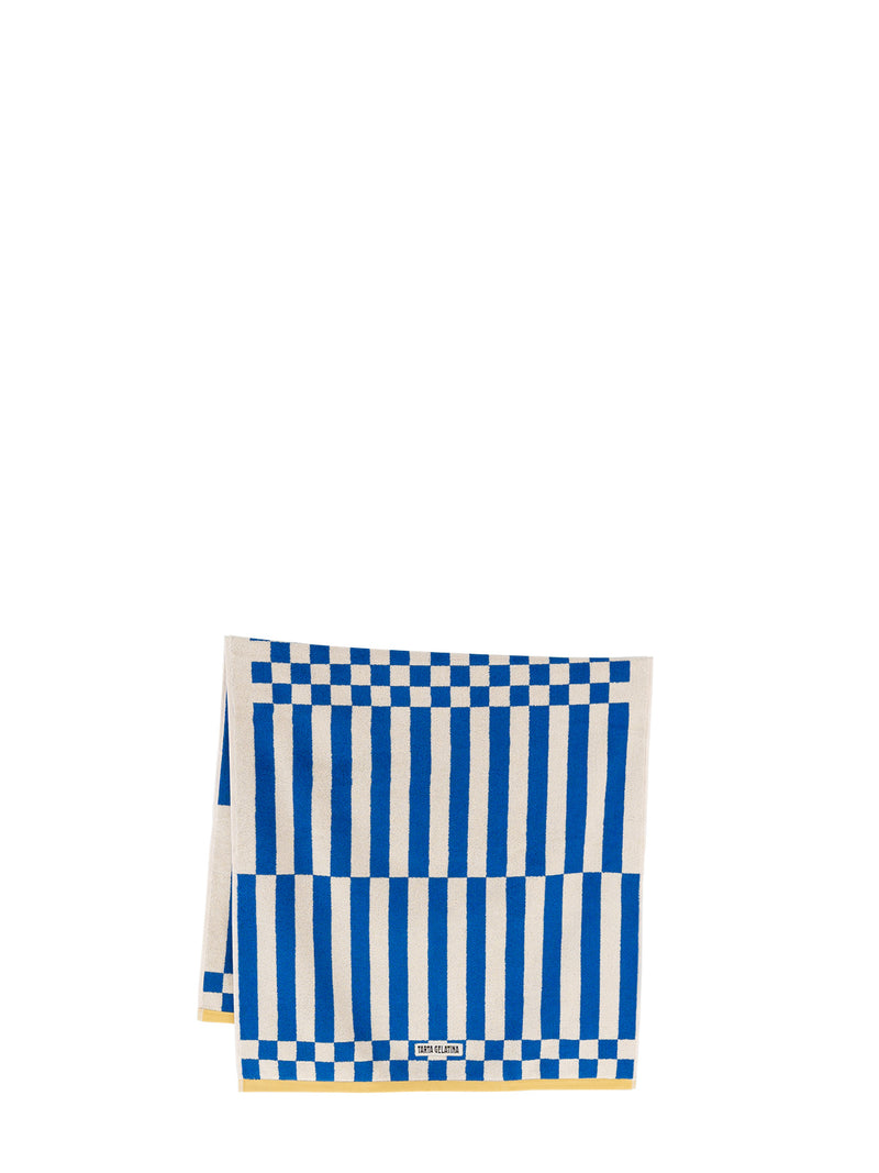 A folded bath towel with a blue and white striped pattern and checkerboard borders, featuring the 'Tarta Gelatina' brand label near on the bottom edge which has a contrasting yellow trim