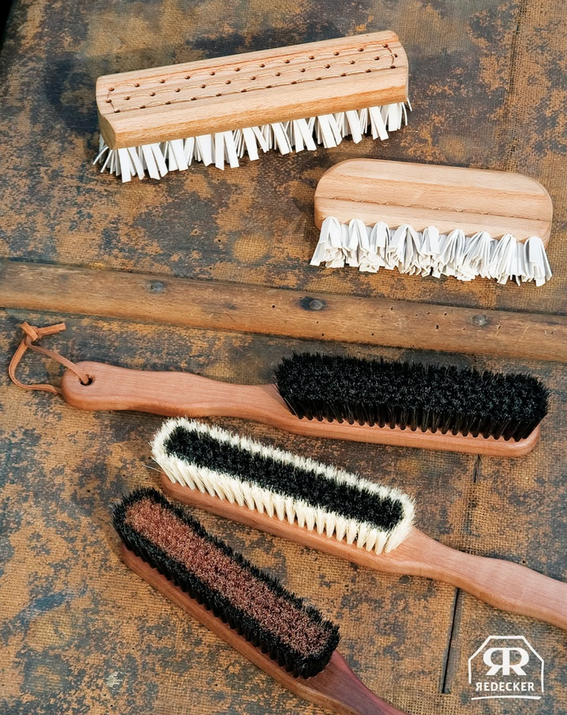 Set of garment brushes with wooden handles and bristle heads on a rustic wooden surface, featuring the Redecker brand.