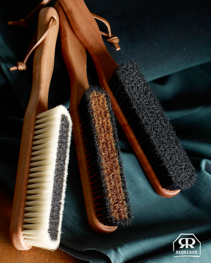 Set of three garment brushes with different bristle types on a dark fabric background, featuring the Redecker brand logo.