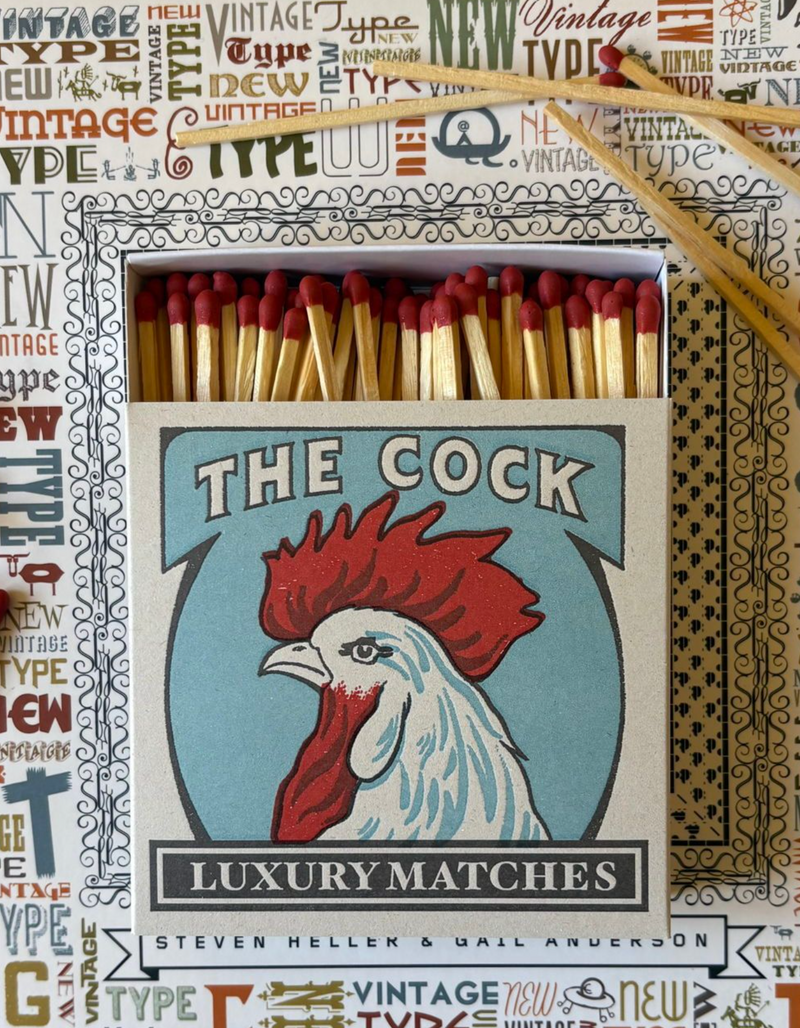 Matchbox with rooster illustration labeled 'The Cock Luxury Matches' on a patterned background.