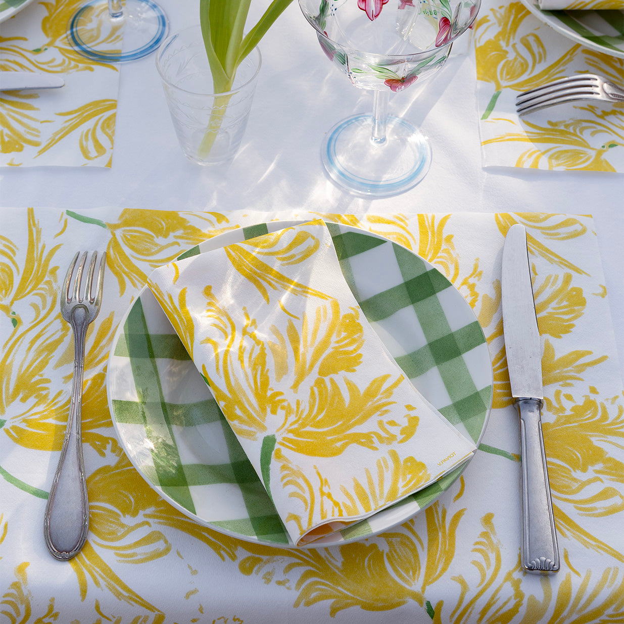 Table setting with yellow and green patterned tablecloth, napkin, and silverware.