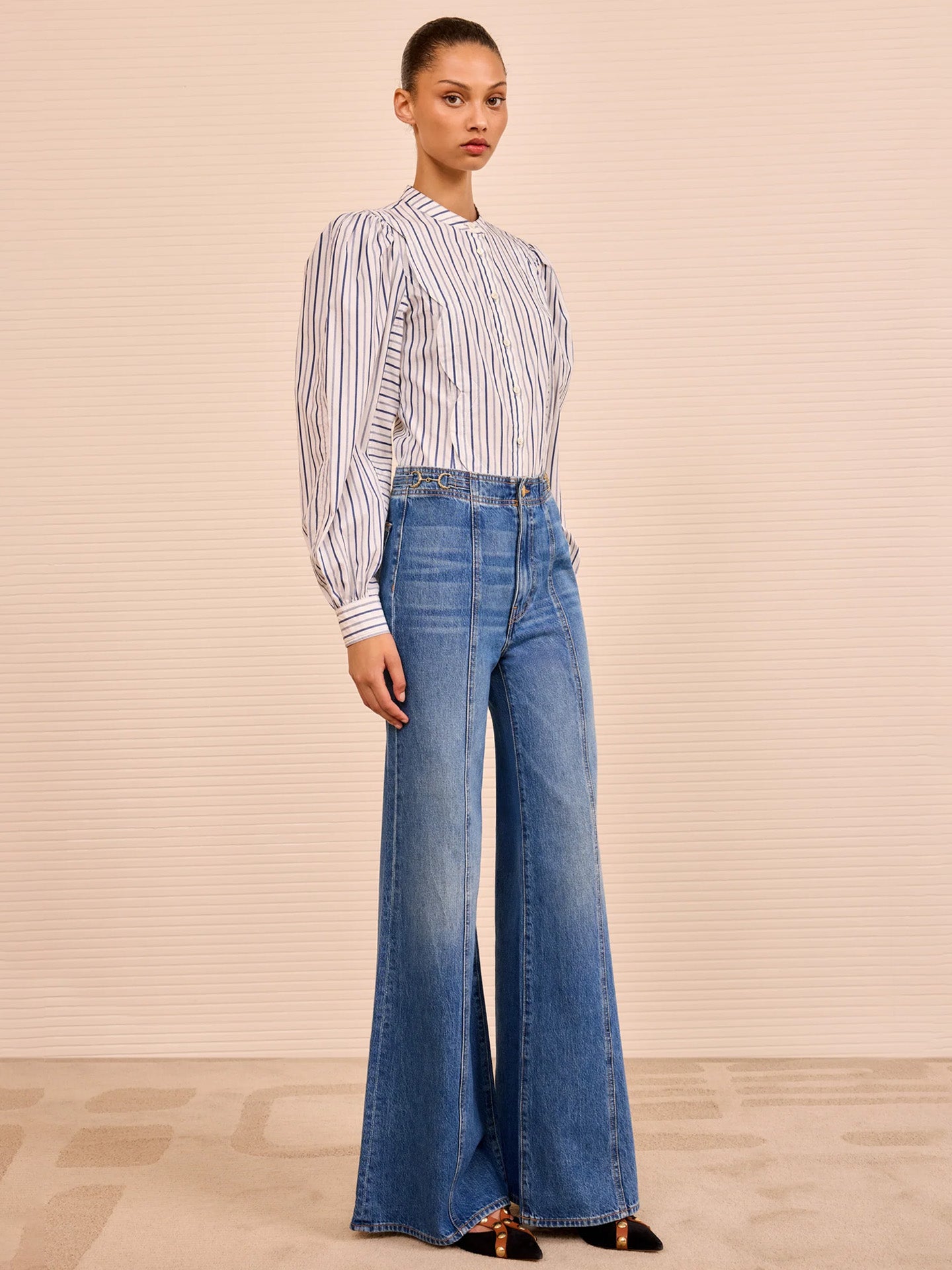 Woman wearing a striped shirt and blue flared jeans against a beige background