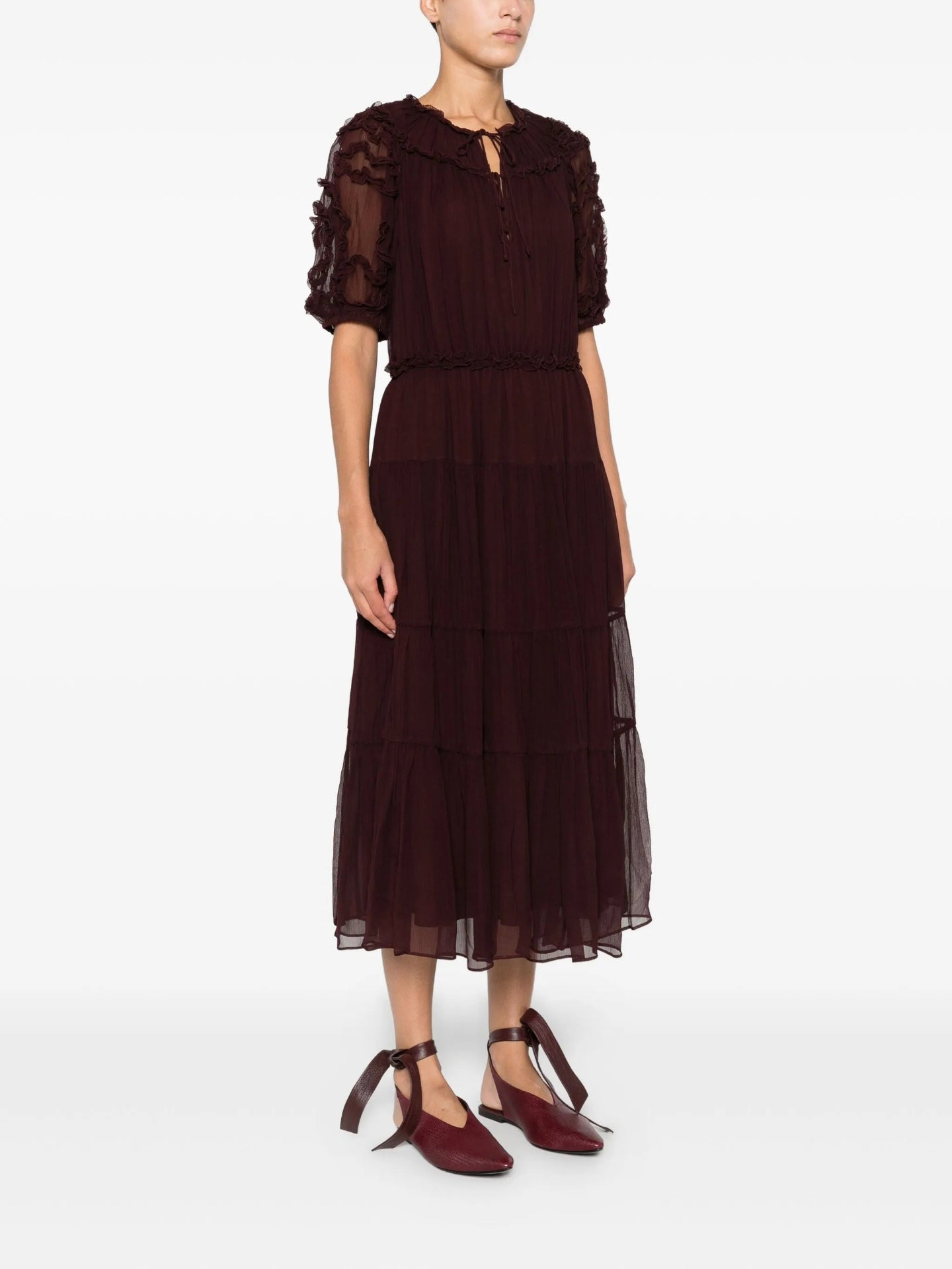 Woman wearing a burgundy dress with sheer sleeves on a white background