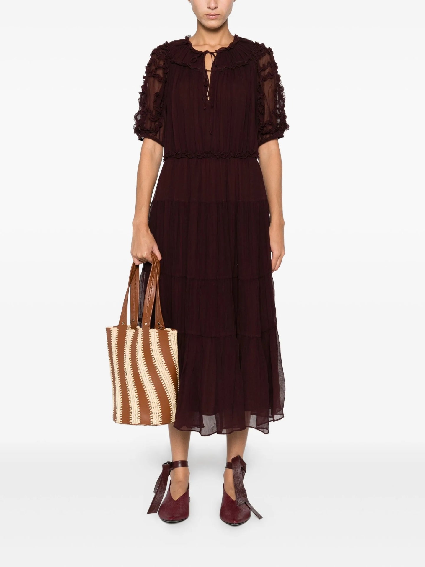 Woman wearing a dark brown dress holding a straw bag on a white background