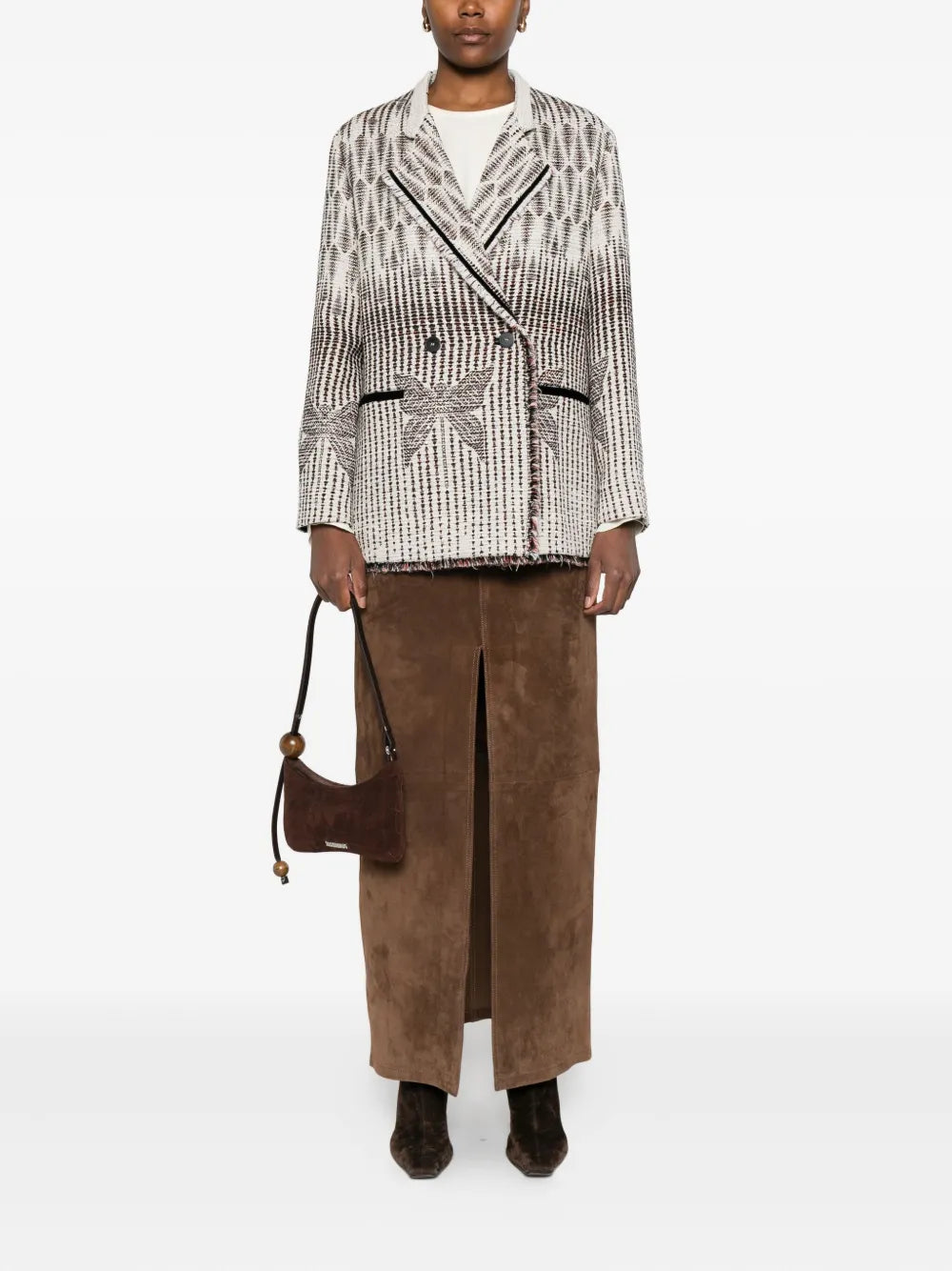 Modelwearing a patterned blazer and brown pants with a brown bag on a white background