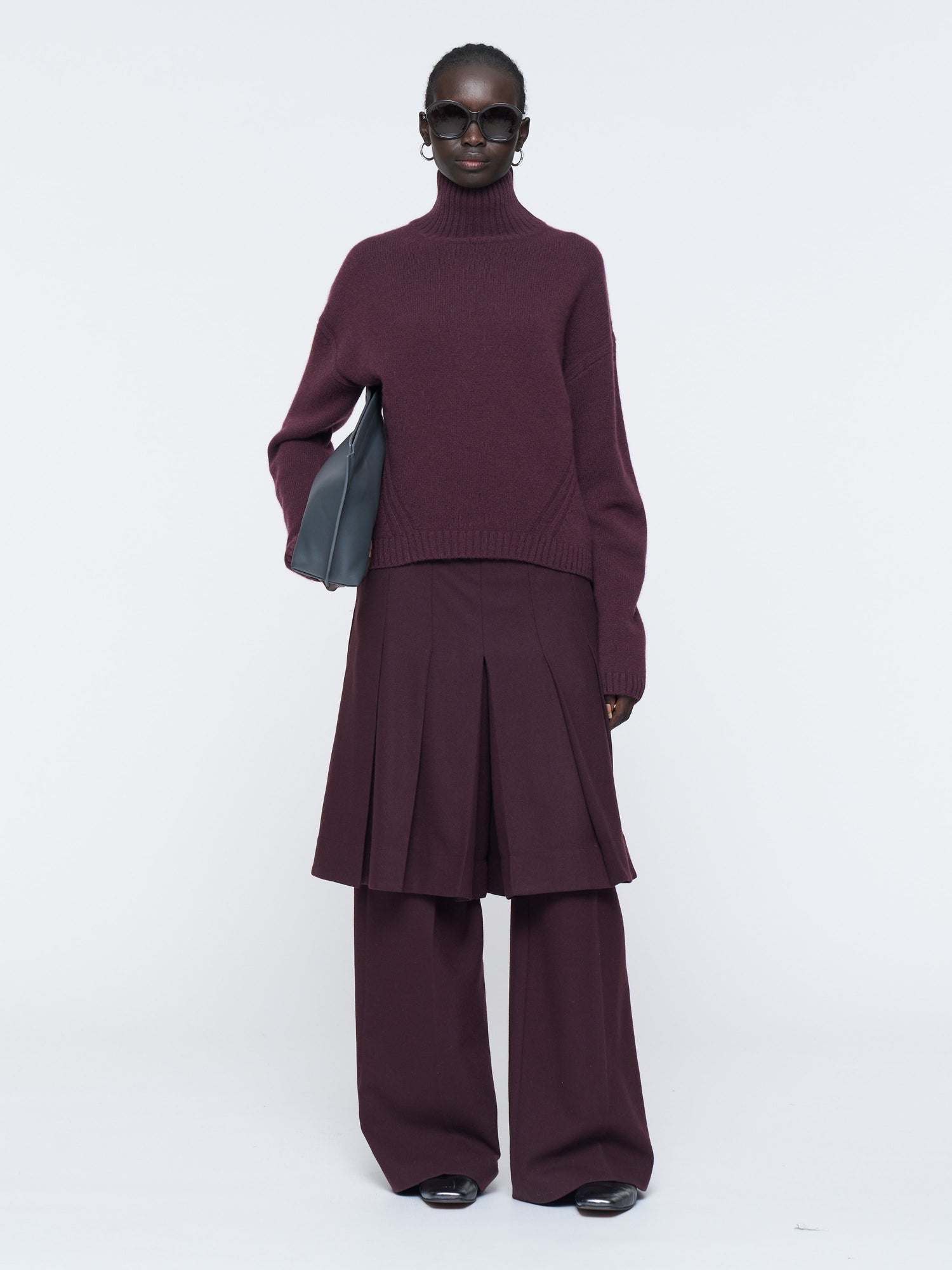 Woman wearing a burgundy outfit with wide-leg pants and a turtleneck sweater on a white background