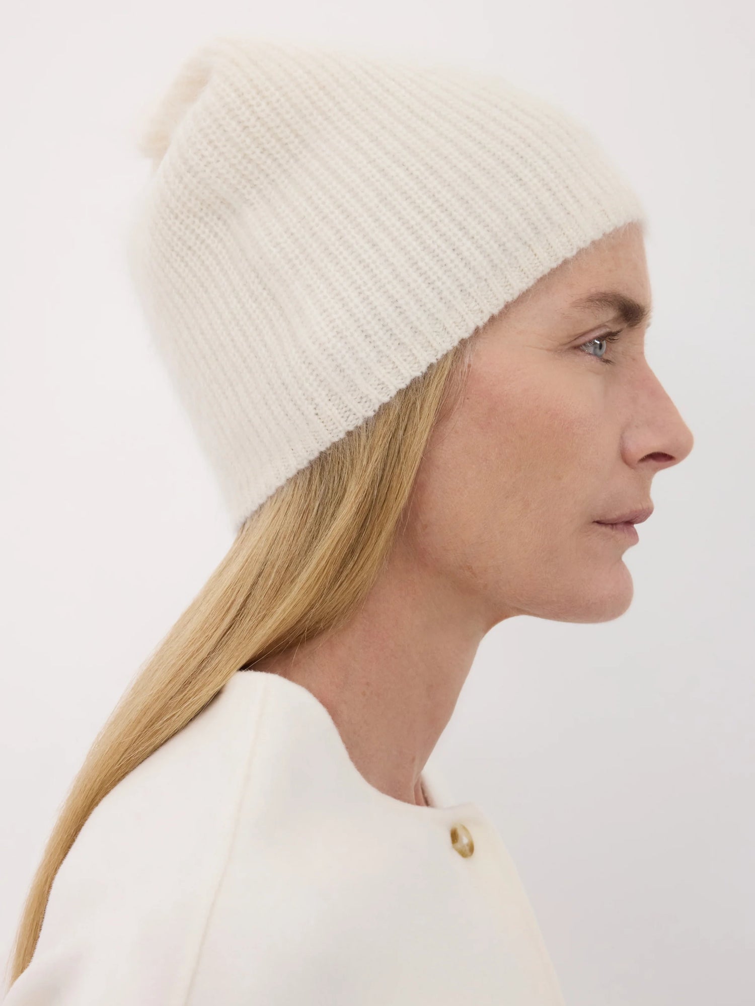 Woman wearing an ivory knit beanie and white top against a plain background