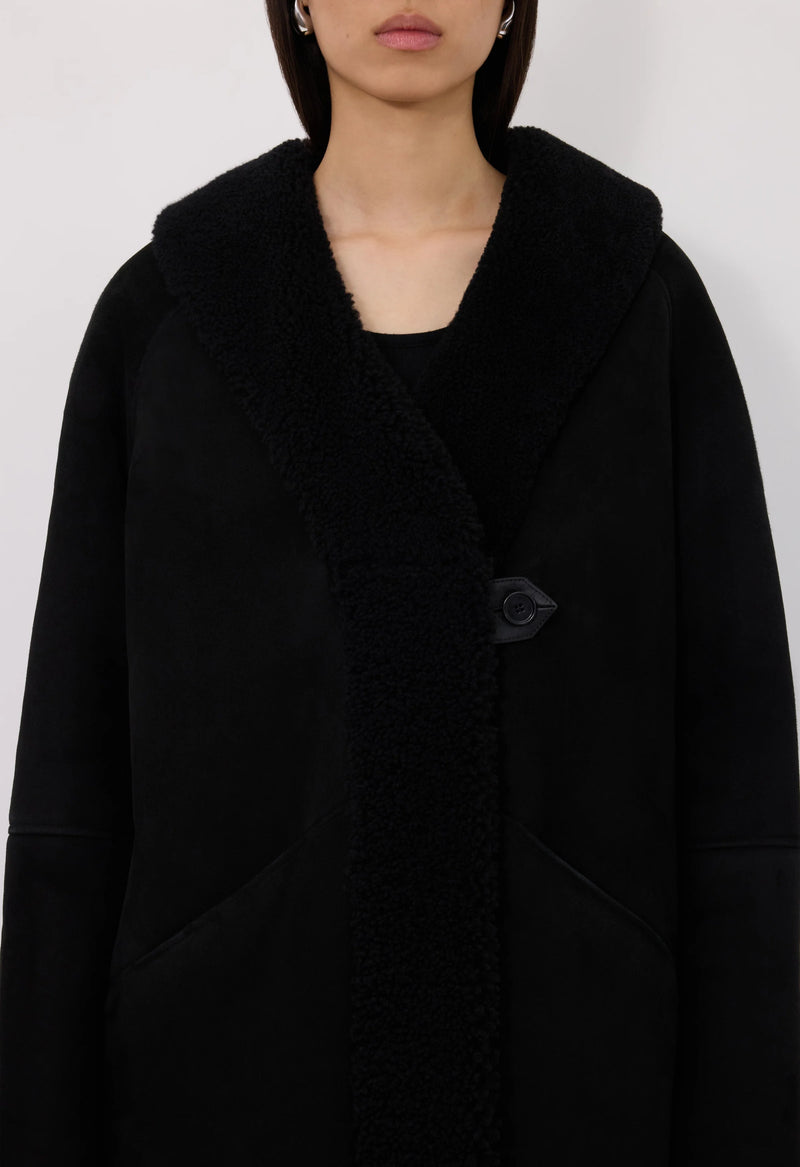 Black shearling coat worn by a person on a white background