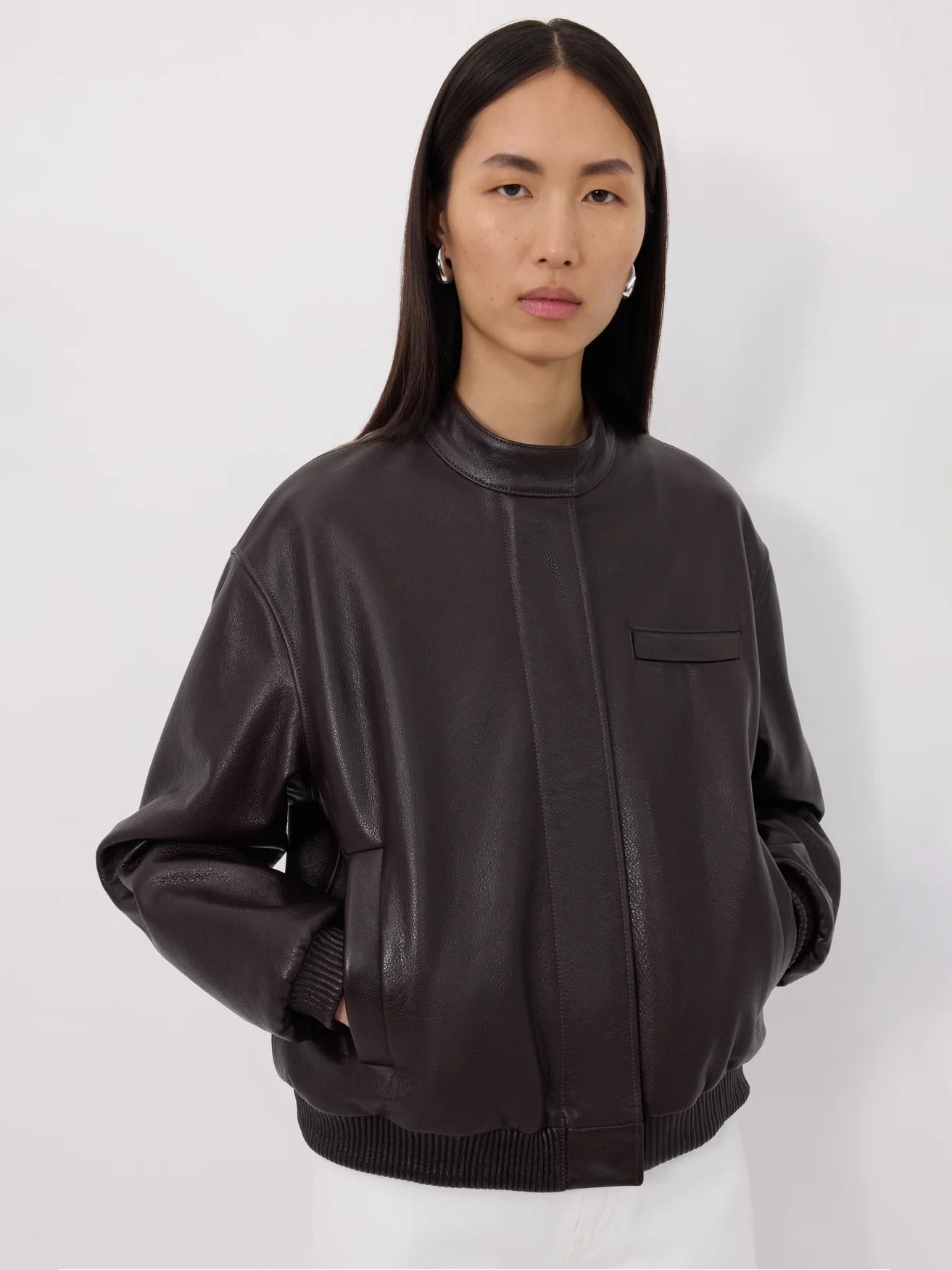 Person wearing a dark brown leather bomber jacket on a white background