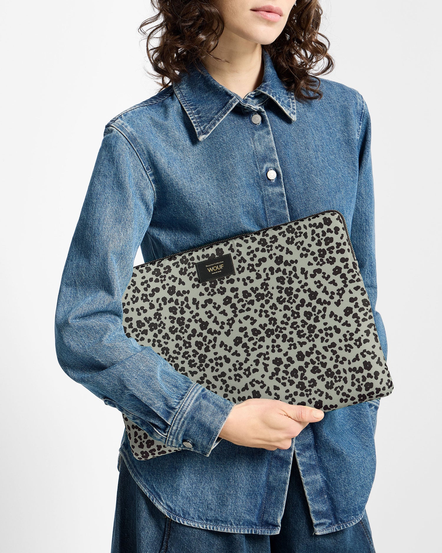 A model wearing a blue denim shirt holds a gray fabric pouch with a black leopard print pattern. The pouch features a small black brand label that reads 'MILY'.