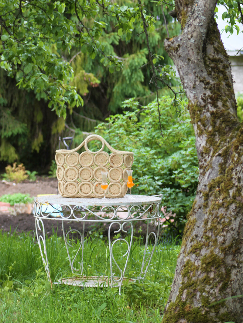 Woven bag on a decorative metal table in a garden setting