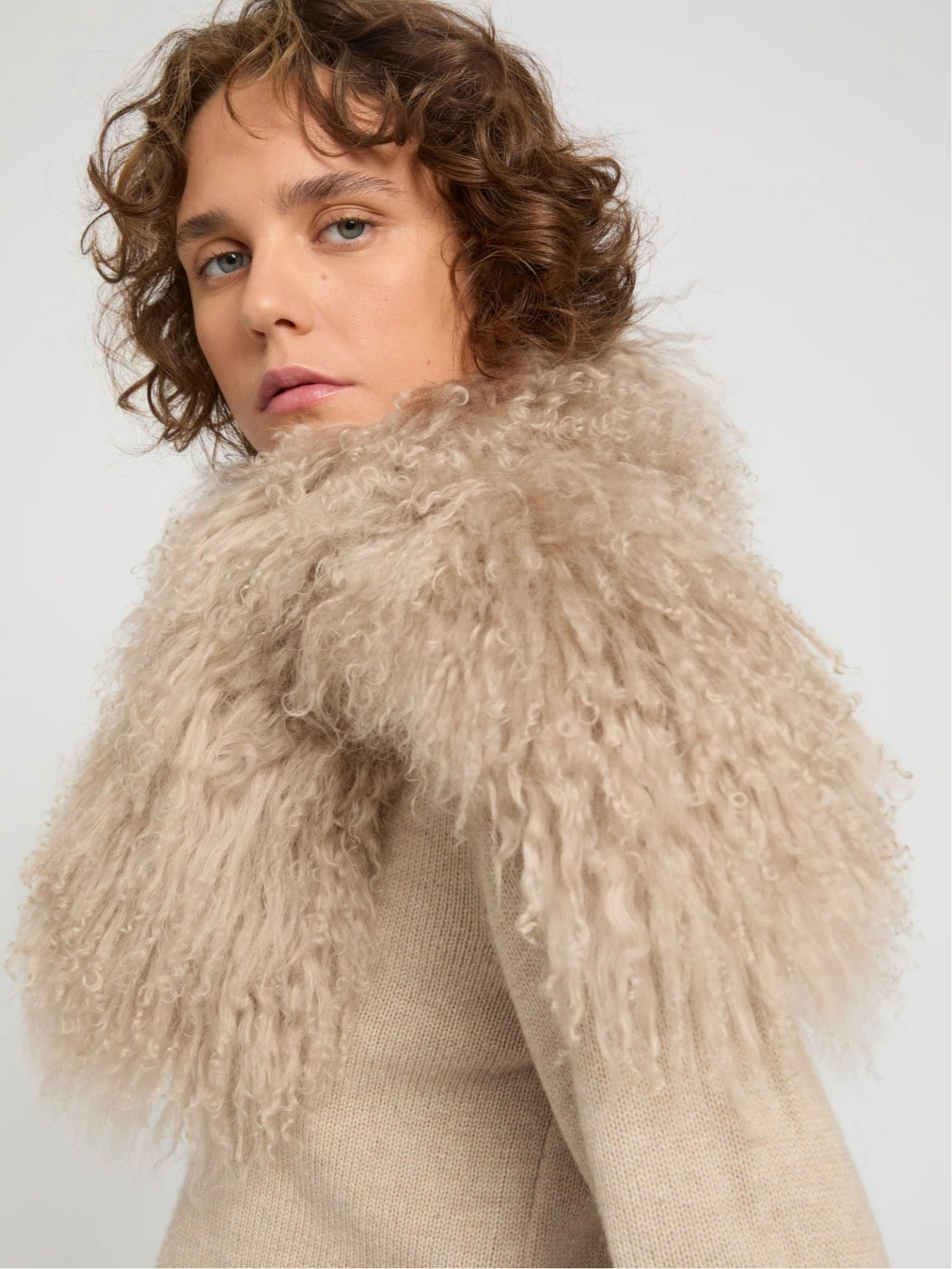 Person wearing a beige fur scarf against a plain background
