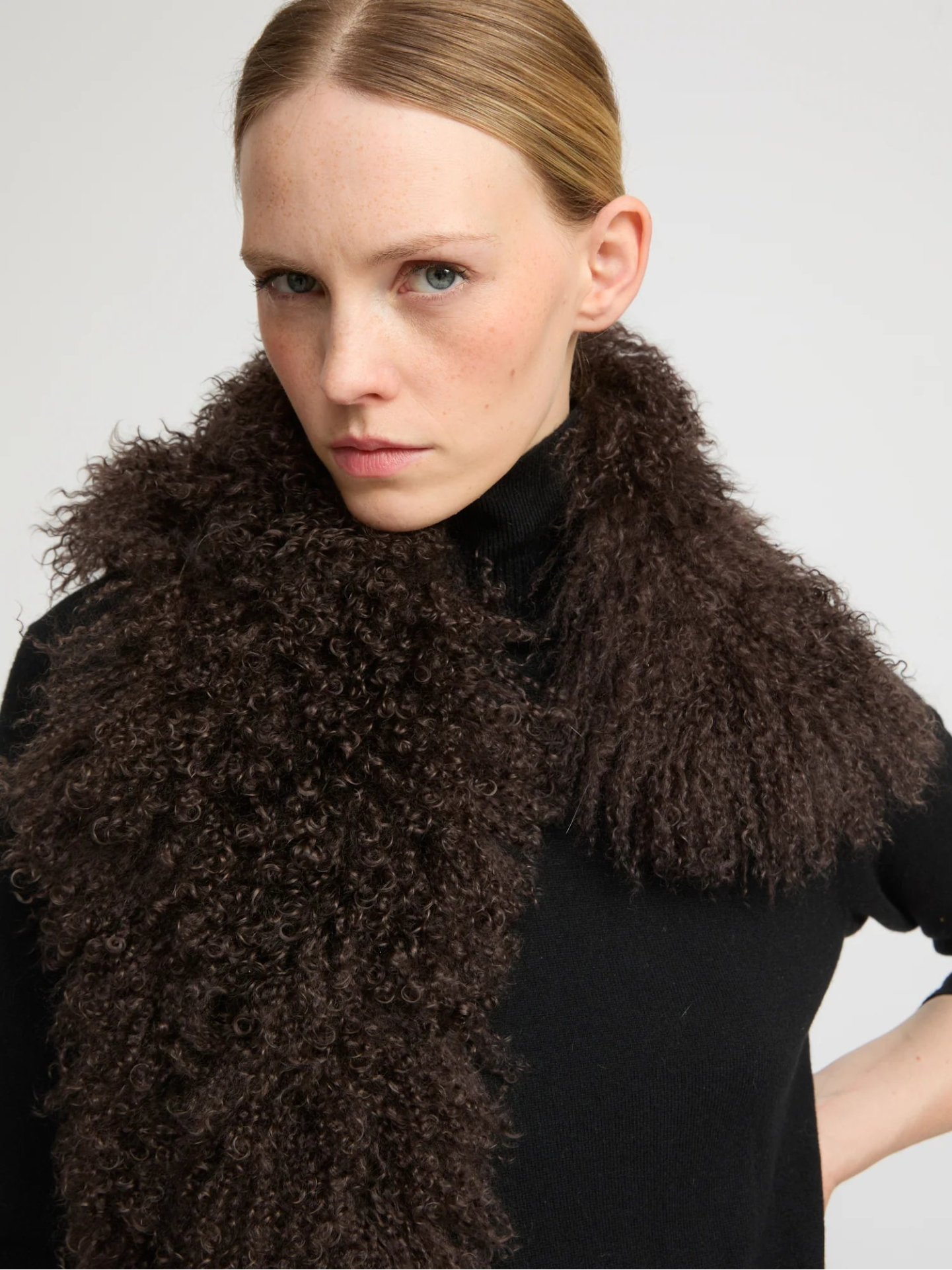 Woman wearing a dark brown lambwool scarf against a plain background