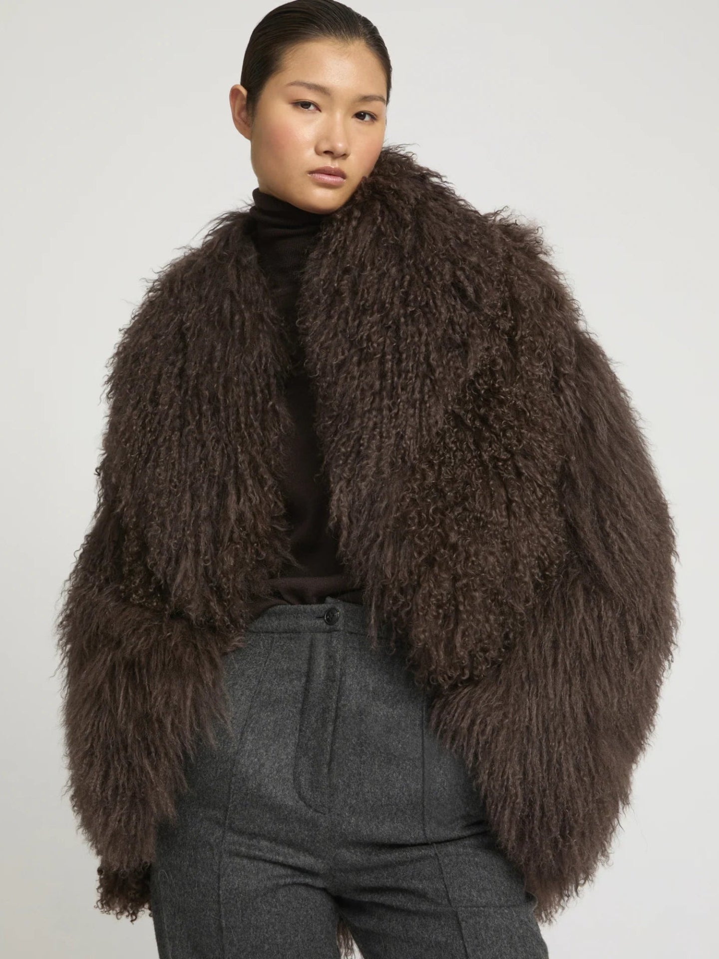 Person wearing a brown fluffy lambwool coat against a plain background