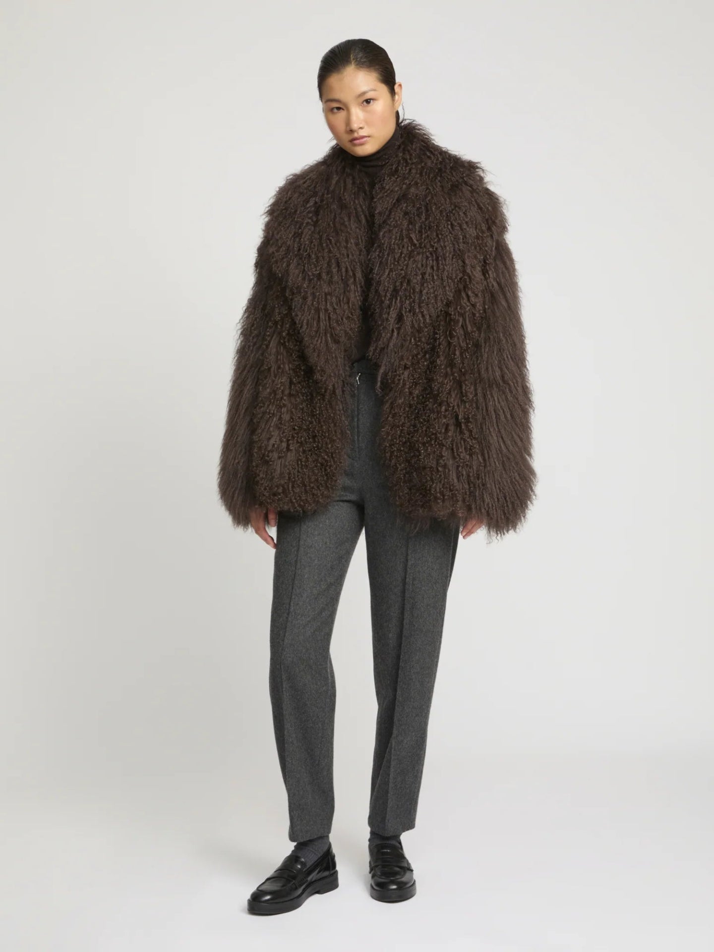 Person wearing a brown fluffy  lambwool coat on a white background