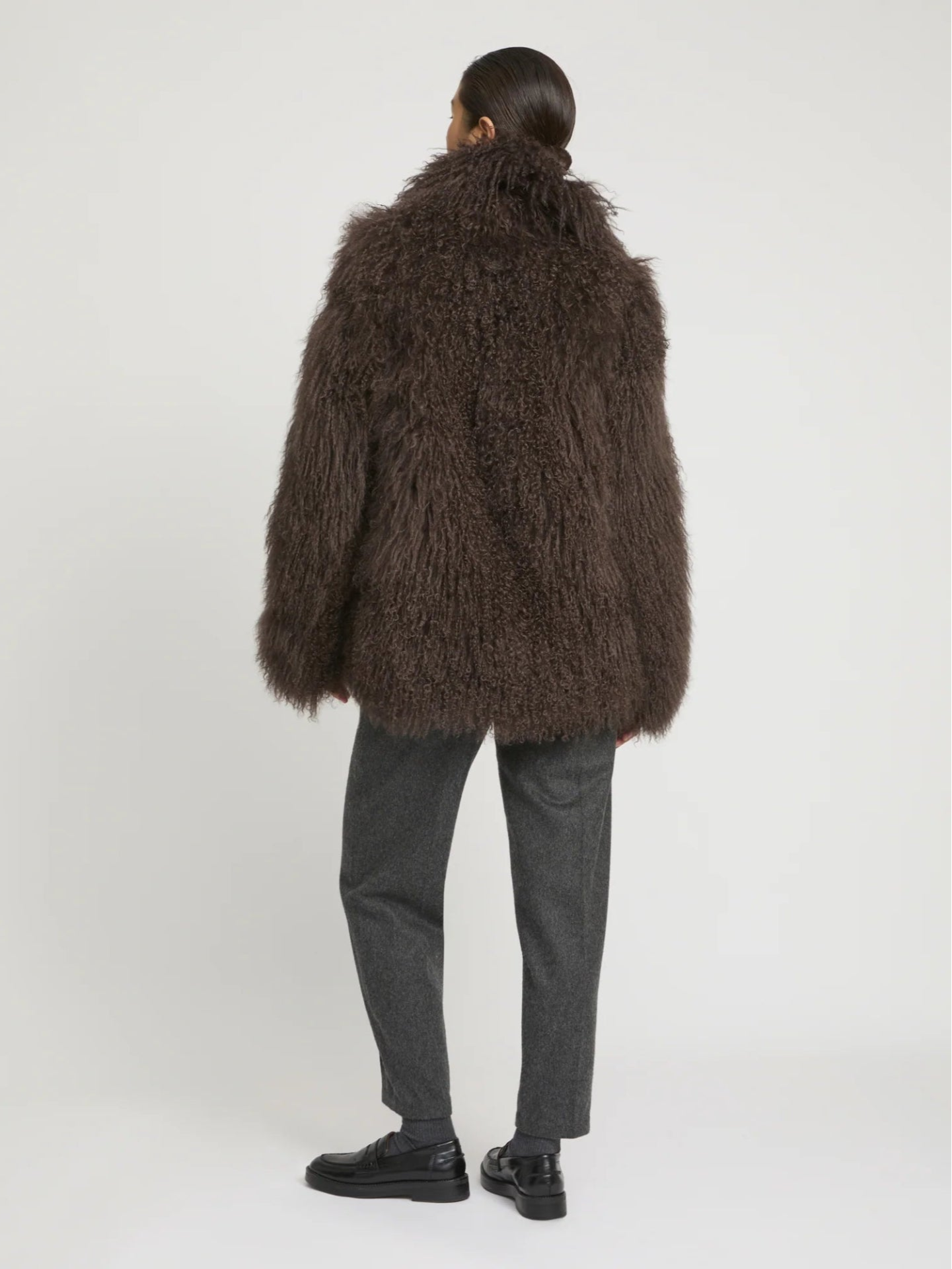 Person wearing a brown fluffy lambwool coat on a white background