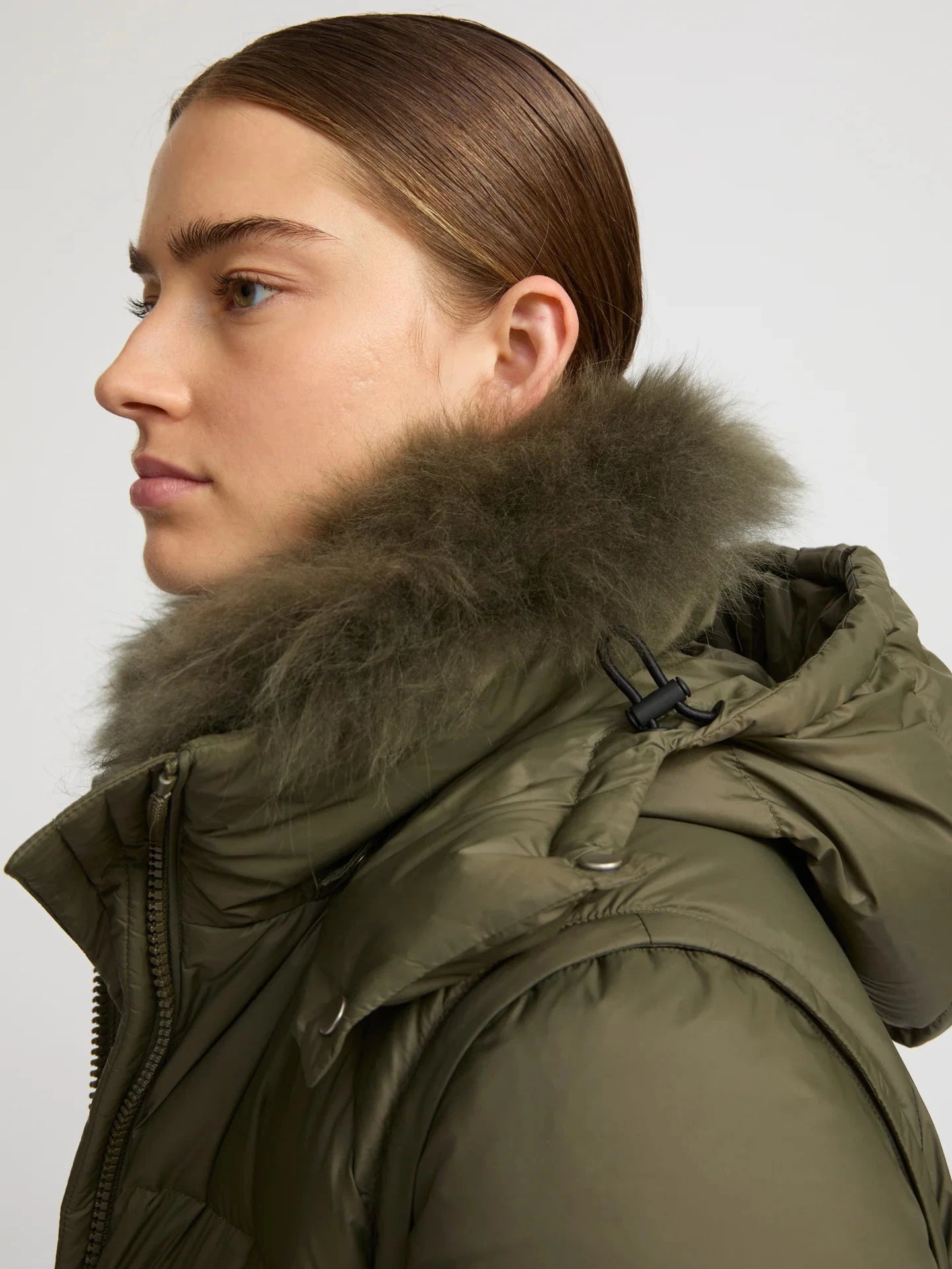 Person wearing a green winter coat with a fur-lined hood on a light gray background