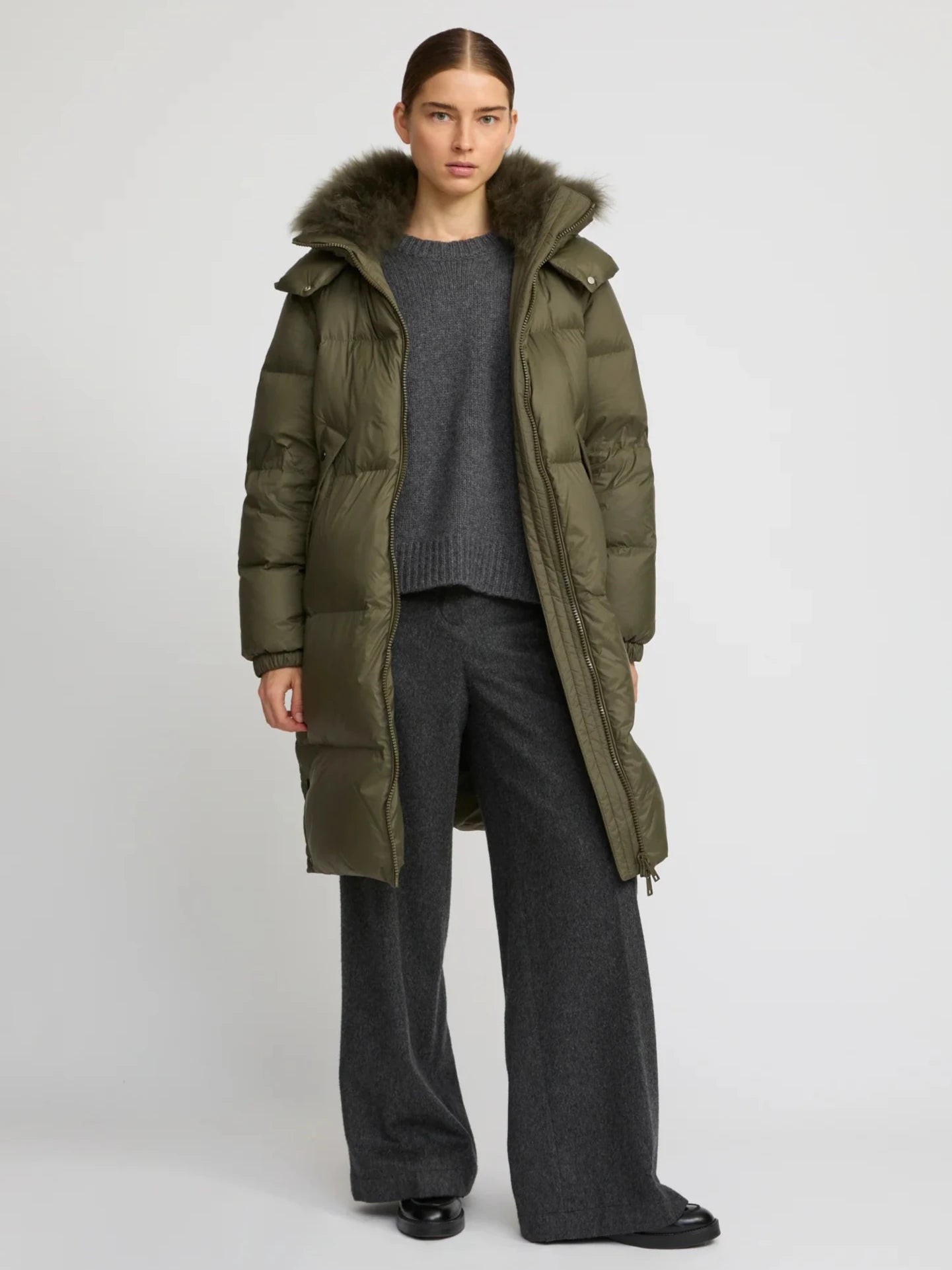 Person wearing a green puffer coat with fur hood on a white background