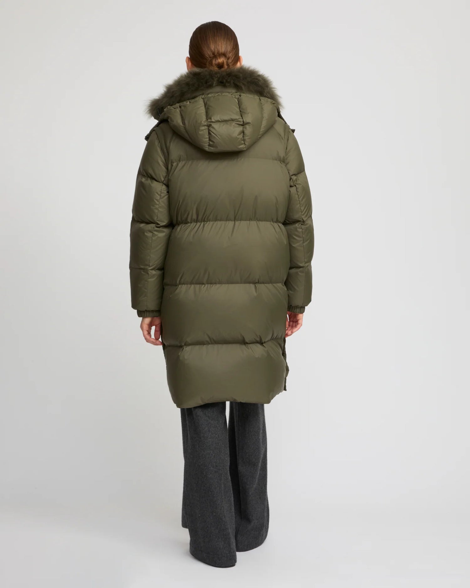 Person wearing a green puffer coat with fur hood on a white background