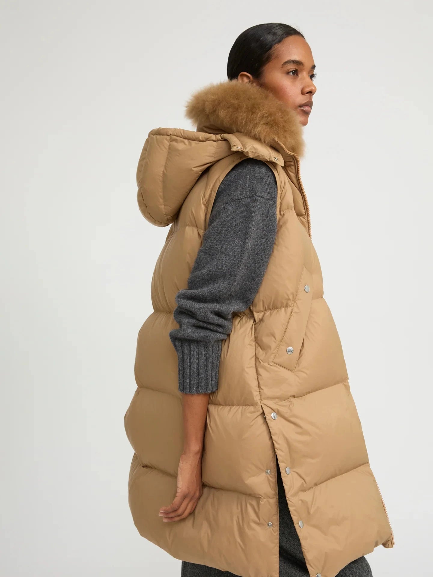 Woman wearing a long beige puffer vest with a fur hood on a white background