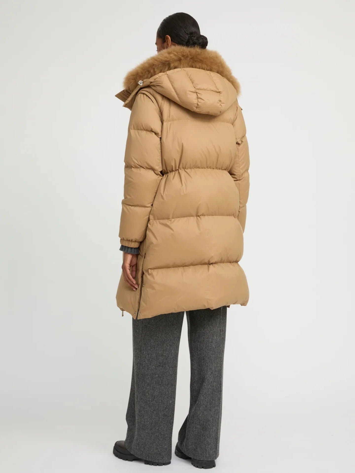 Person wearing a beige puffer jacket with fur hood on a white background