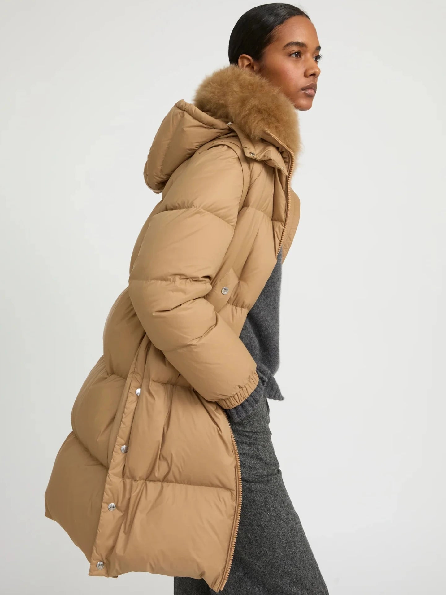 Woman wearing a beige puffer jacket with fur hood on a white background