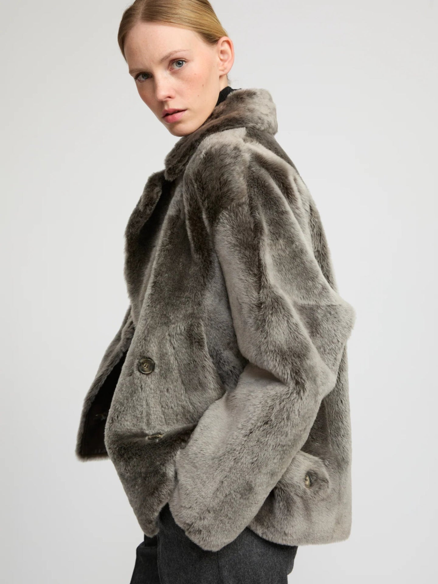 Woman wearing a grey lambwool coat on a plain background