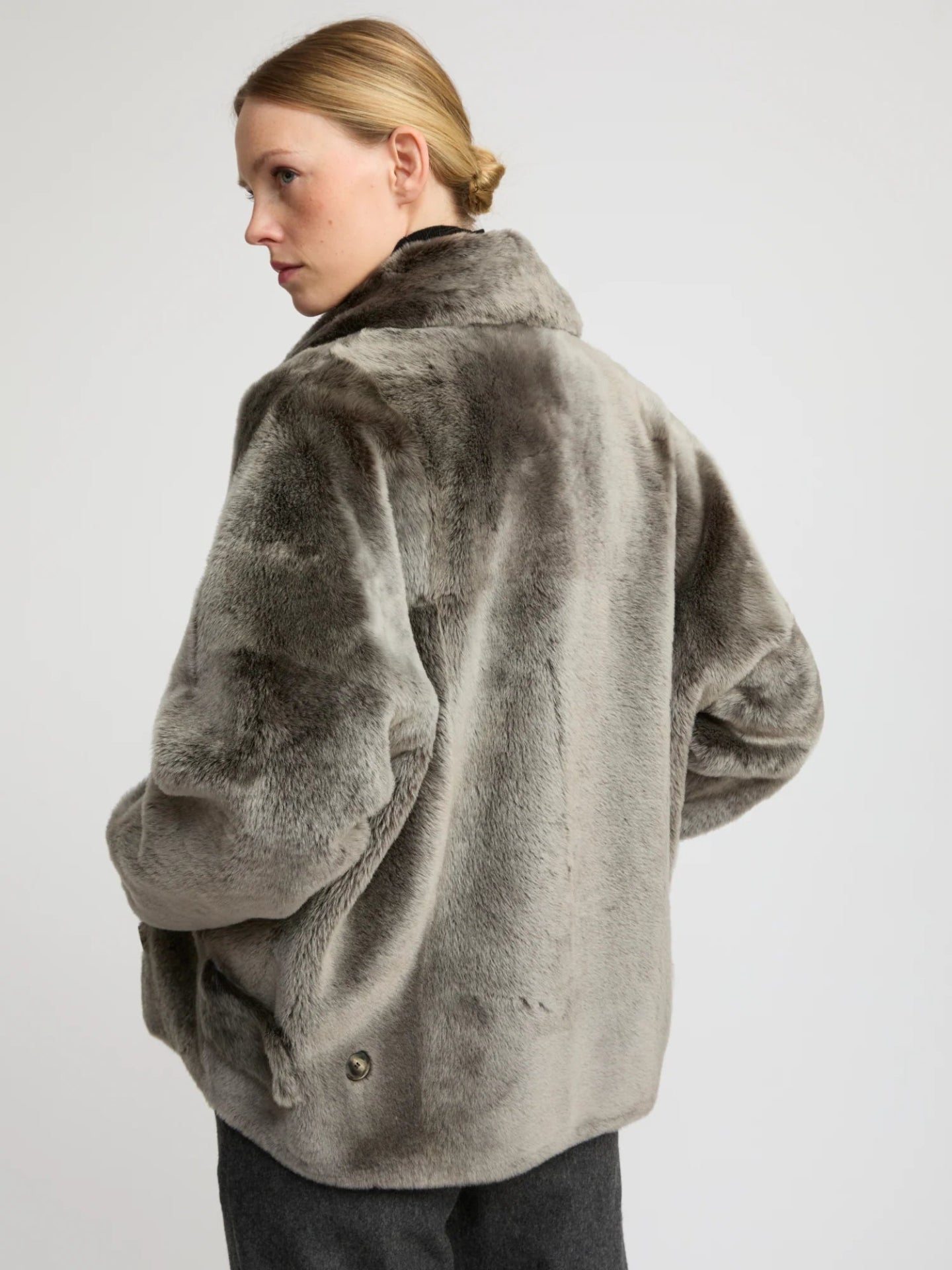 Person wearing a gray lamb fur jacket on a plain background
