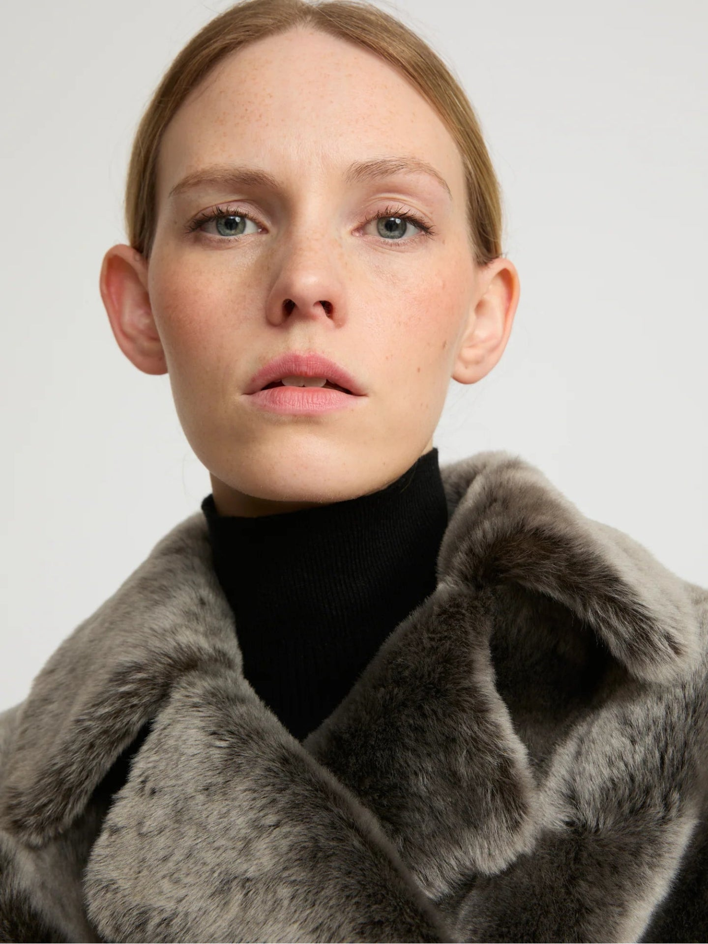 Woman wearing a grey lamb fur coat against a plain background
