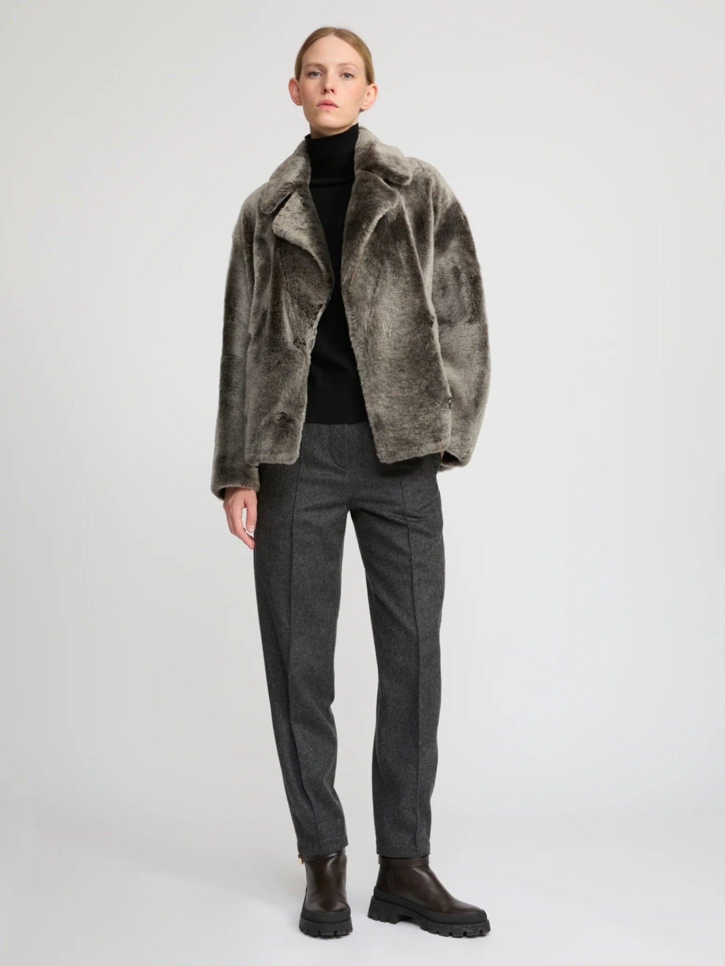 Person wearing a gray fur coat, black turtleneck, gray pants, and black boots on a white background