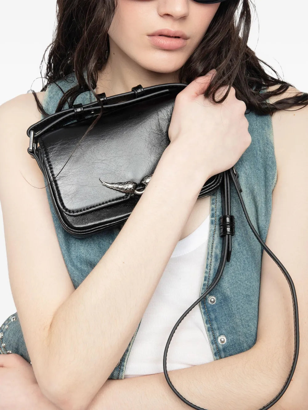 Person holding a black handbag with a long strap against a neutral background